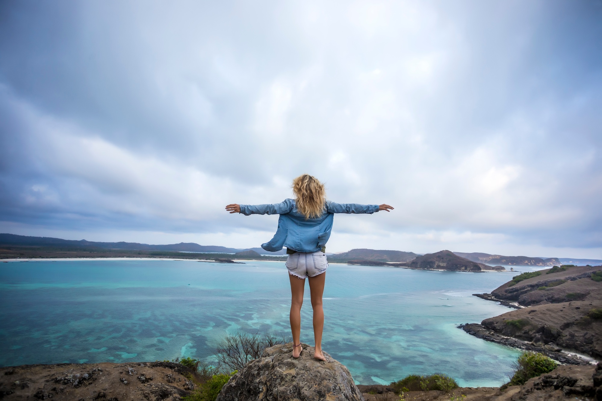 Indonesia, Lombok, woman standing at the coast with outstretched arms