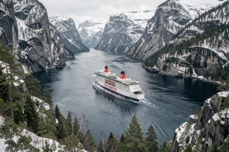 Ferry Hurtigruten naviguant dans un fjord norvégien entouré de falaises enneigées et de forêts de pins