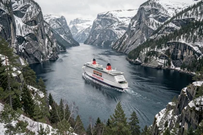 Ferry Hurtigruten naviguant dans un fjord norvégien entouré de falaises enneigées et de forêts de pins